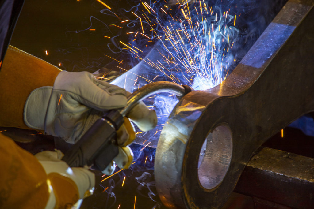 Close up of MIG gun with sparks welding on heavy equipment part