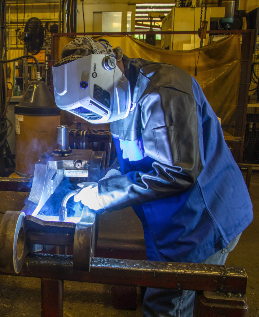 Side view of welder welding on heavy equipment part 