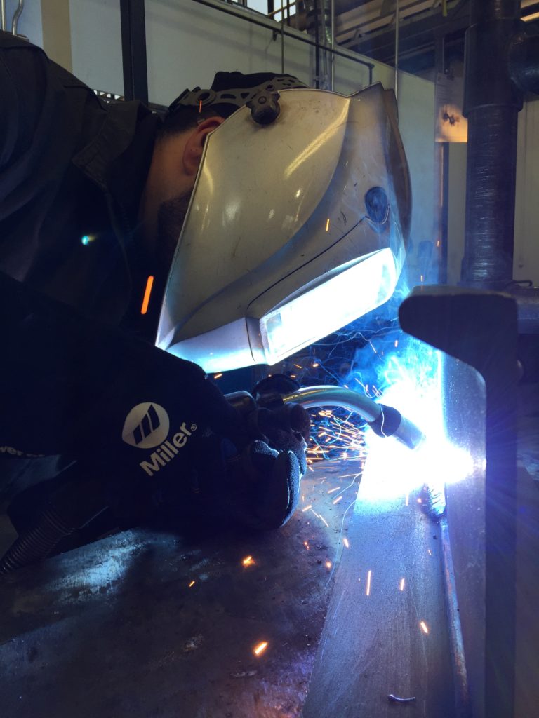 Closeup side view of welder welding on part on a table