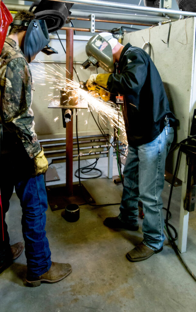 Welding student grinding a part while another student watches